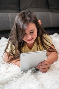 Adorable little girl using a digital tablet on the floor at home. High quality photography. Adorable little girl using a digital tablet on the floor at home.