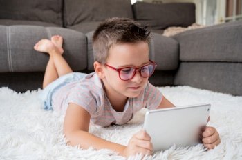 Adorable little boy using a digital tablet on the floor at home. High quality photography.. Adorable little boy using a digital tablet on the floor at home.