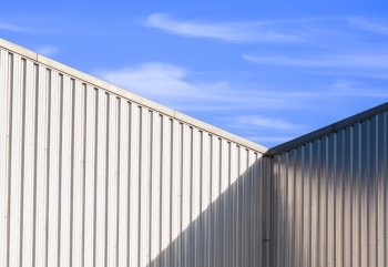 Sunlight and shadow on surface of corrugated steel wall of warehouse building against blue sky background in perspective view