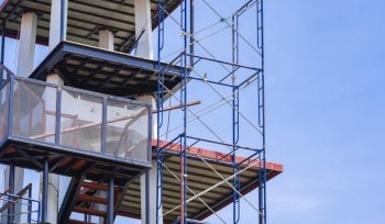 Low angle view of scaffolding with metal staircase structure outside of the old tower in construction site against blue sky background, renovation and improvement concept