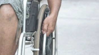 Focus at disabled man's hand manually pushing wheelchair on pavement in public park, close up with copy space