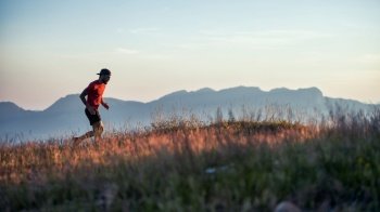 In a hilly sunset in colorful meadows a young sporty man runs alone