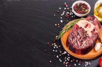 Fresh raw meat beef steak with bone with spices, rosemary, tomatoes, garlic and olive oil on wooden cutting board and on the black slate surface. cooking ingredients. Top view. Flat lay.. Cooking ingredients. Fresh raw meat beef steak with bone.
