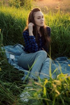 Portrait of a beautiful young woman on meadow watching the sunset enjoying nature summer evening outdoors.