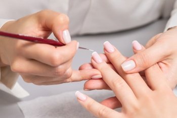 Hand of young woman receiving french manicure by beautician at nail salon.. Woman receiving french manicure by beautician