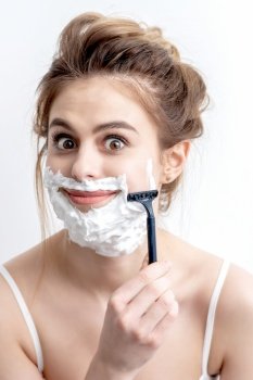 Beautiful young caucasian woman shaving her face by razor on white background. Pretty woman with shaving foam on her face. Woman shaving her face by razor