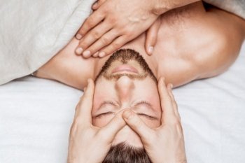 Top view of relaxing young caucasian man enjoying head massage by two masseurs. Young caucasian man enjoying head massage