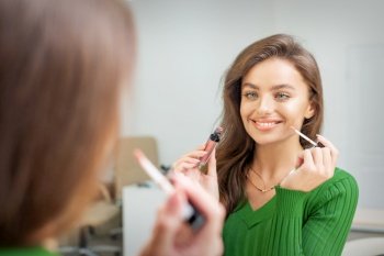 Beautiful young caucasian smiling woman applying gloss to the lips looking in the mirror. Woman applying gloss to the lips