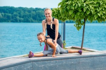 Mother and daughter doing gym exercises on the grass at the pier of the river. Mother and daughter doing gym exercises