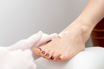 Pedicurist in white gloves massaging cream into woman leg in beauty salon. Pedicurist in white gloves massaging cream