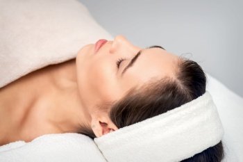 Side view of young woman lying on beautician table with closed eyes while waiting for cosmetic procedure in beauty salon. Young woman waiting for cosmetic procedure