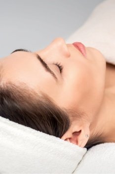 Side view of young woman lying on beautician table with closed eyes while waiting for cosmetic procedure in beauty salon. Young woman waiting for cosmetic procedure