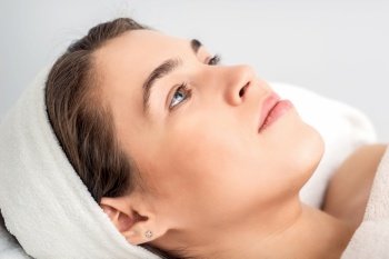 Side view portrait of pensive young woman lying on beautician table while waiting for cosmetic procedure in beauty salon. Young woman waiting for cosmetic procedure