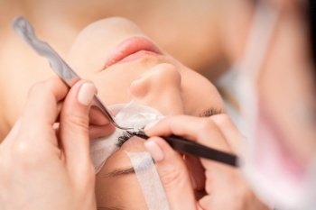 Young caucasian woman receiving eyelash extensions procedure in beauty salon. Woman receiving eyelash extensions procedure
