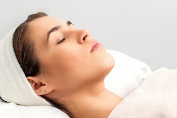 Side view of young woman lying on beautician table with closed eyes while waiting for cosmetic procedure in beauty salon. Woman waiting for cosmetic procedure