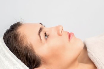 Side view portrait of pensive young woman lying and waiting for cosmetic procedure in beauty salon. Woman waiting for cosmetic procedure