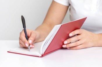 Young female hand writes notes to notebook planning her schedule at white table. Hand writing notes to notebook