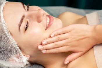Beautiful young woman lying and touching face skin after cosmetic procedures in spa. Woman lying and touching face skin