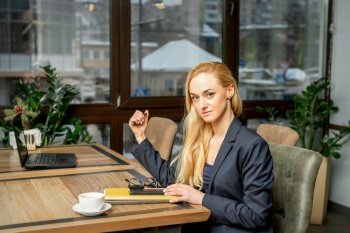 Portrait of a young caucasian businesswoman with documents and laptop at the table looking at the camera in cafe. Portrait of a young businesswoman