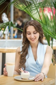 A beautiful young caucasian woman sitting at the table with cakes and a cup of coffee in cafe outdoor. Beautiful young woman drink coffee