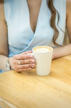 Female hands with cup of coffee on the background of a wooden table in a cafe. Female hands with cup of coffee