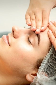 Young caucasian woman receiving facial massage by beautician’s hands in spa medical salon. Young woman receiving facial massage