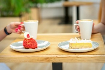 Two young girlfriends drinking coffee with pieces of cake sitting at the table in a cafe outdoors. Two young girlfriends drinking coffee