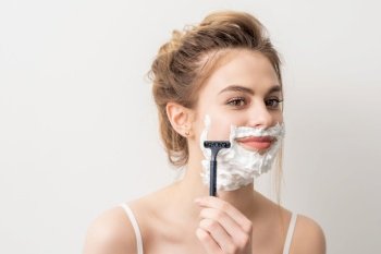 Beautiful young caucasian smiling woman shaving her face with razor on white background. Woman shaving face with razor