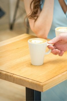 Hand of waiter puts a cup of coffee latte on the wooden table in a cafe. Waiter puts a cup of coffee