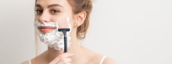Beautiful young caucasian smiling woman shaving her face with razor on white background. Woman shaving face with razor