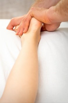 Male massage therapist massaging foot of young woman in spa beauty salon. Masseur massaging foot of woman