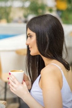 The side view of a young woman drinking coffee resting at the resort at a cafe outdoors. The side view of a young woman drinking coffee resting at the resort at a cafe outdoors.