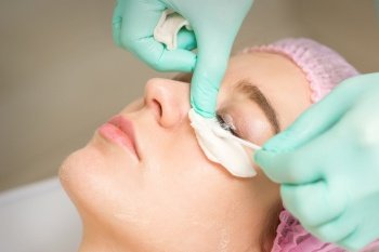 Young woman receiving eyelash removal procedure and removes mascara with a cotton swab and stick in a beauty salon. Young woman receiving eyelash removal procedure and removes mascara with a cotton swab and stick in a beauty salon.