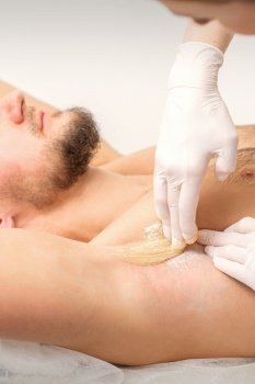 Young caucasian man receiving hair removal from his armpit in a beauty salon, depilation men’s underarm. Young caucasian man receiving hair removal from his armpit in a beauty salon, depilation men’s underarm.