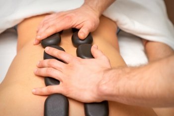 Young caucasian woman receiving back massage with black stones by masseur in spa salon. A woman getting a spa treatment. Young caucasian woman receiving back massage with black stones by masseur in spa salon. A woman getting a spa treatment.