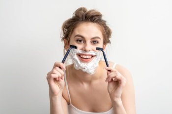 Beautiful young caucasian woman shaving her face by razor on white background. Pretty smiling woman with shaving foam and razor on her face. Beautiful young caucasian woman shaving her face by razor on white background. Pretty smiling woman with shaving foam and razor on her face.