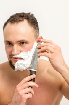 Young caucasian man shaving beard with a big knife on white background. Young caucasian man shaving beard with a big knife on white background.