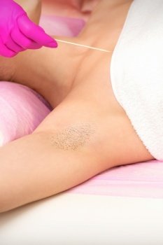 Hand in glove with spatula depilates female hairy armpit in a spa. Hand in glove with spatula depilates female hairy armpit in a spa.