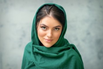 Portrait of a pretty young caucasian woman with makeup in a green headscarf on gray background. Portrait of a pretty young caucasian woman with makeup in a green headscarf on gray background.