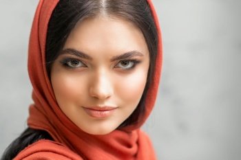 Portrait of a pretty young caucasian woman with makeup in a red headscarf on gray background. Portrait of a pretty young caucasian woman with makeup in a red headscarf on gray background.