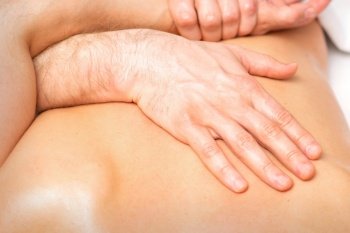 A male physiotherapist stretches the arms on the back of a man lying down, close up. A male physiotherapist stretches the arms on the back of a man lying down, close up.
