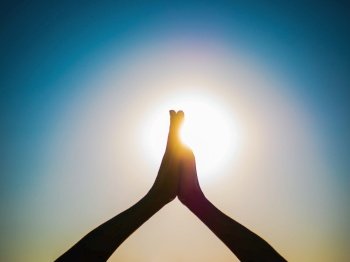 Woman’s hands symbolizing prayer and gratitude. Mudra. Yoga concept. Silhouette of female hands on sun background. Beautiful scene