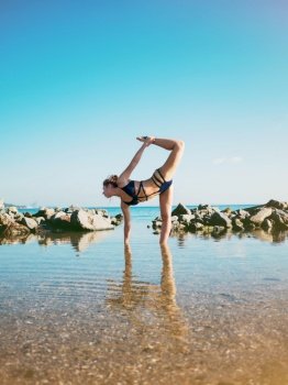 Young caucasian woman in swimsuit practicing yoga in sea water, lake or river. Beautiful reflection. Complex asanas, balance. Fitness, sport, yoga and healthy lifestyle concept.