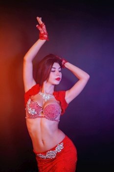 Woman in exotic shining red costume sexually moves her body. Sexy traditional oriental belly dancer girl dancing on neon smoke background. Muslims, temptation concept. Woman in exotic shining red costume sexually moves her body. Sexy traditional oriental belly dancer girl dancing on neon smoke background. Muslims, temptation concept.