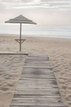 A straw beach umbrella on a sandy beach by the sea.  Cloudy and moody sunset in Furadouro beach, a tourist seaside part of the municipality Ovar, Aveiro, Portugal, Europe.