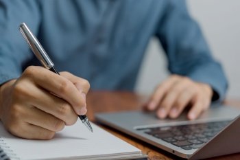 Man Writing with Pen on Notebook and laptop on desk. Business Success, and Effective Planning management and productivity in office environment.