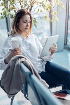 Young traveling woman with a tablet and coffee waiting for a flight in the departure hall at the airport.