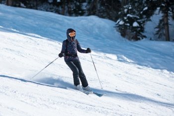 Amateur female skier sliding down the slope on a sunny day at a mountain resort.