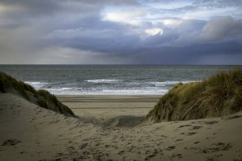 the access to the beach at the top on the island of Texel in the Netherlands with the dunes with the horizon and the dark clouds in the background. the entrance to an empty beach with the sea and the horizon in the background