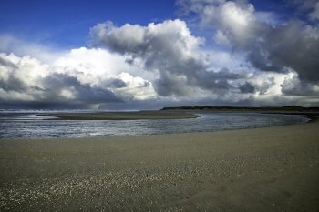 the beach of the island of Texel with dark clouds in the background and a cove with a sandbar in the middel. the sand on the beach and sky and Horizon in the background
